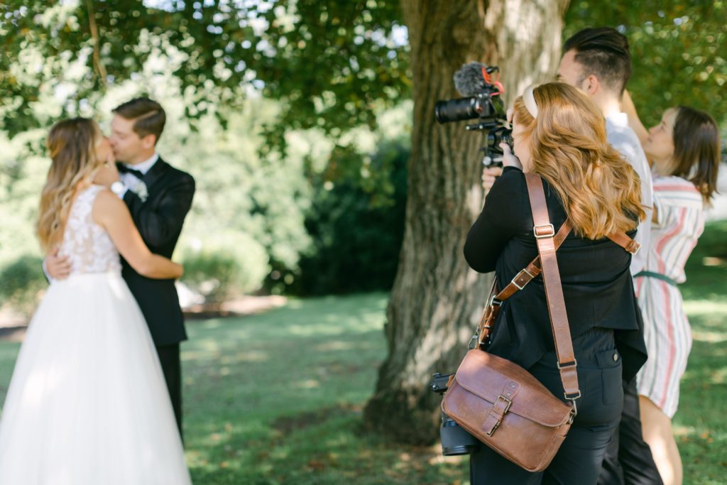 Wedding photographer capturing photos of couple at wedding with camera wearing a messenger bag